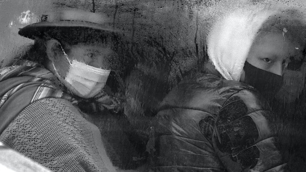 Two people with masks on look through a window dripping with moisture.
